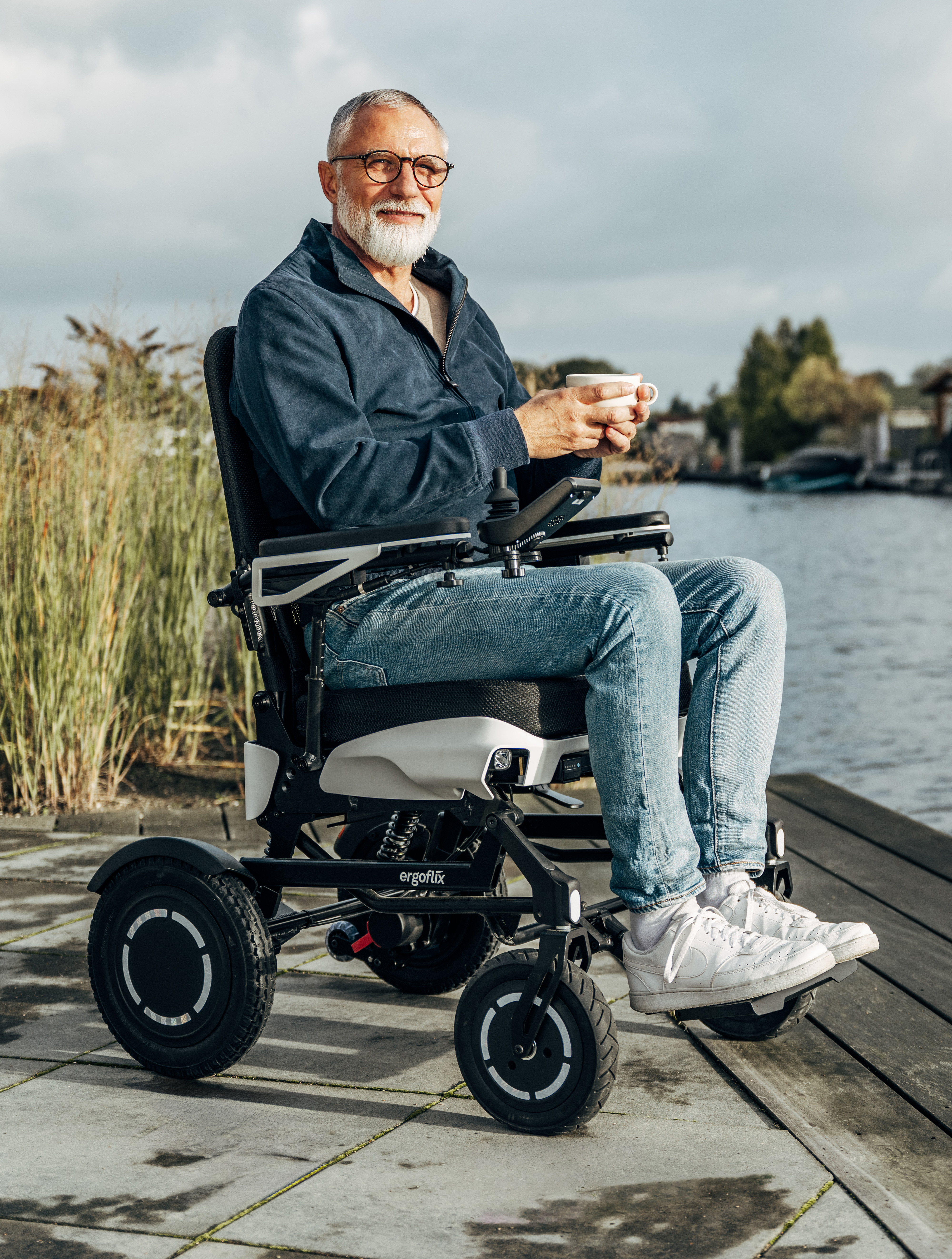 Das Bild zeigt einen Mann im ergoflix vario, der sich am Ufer eines Gew&auml;ssers befindet und eine Tasse Kaffee in der Hand h&auml;lt.